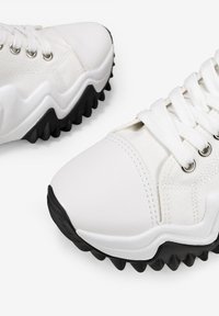 Scarpe da atletica bianche che presentano un mix di materiali sintetici lisci e tela testurizzata, punta rotonda, suola in gomma nera a contrasto e occhielli in metallo.
