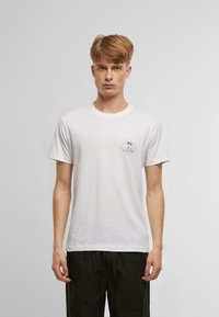 T-shirt en coton blanc avec un petit graphique bleu représentant des palmiers et le mot "FOREVER" à l'intérieur d'une forme de diamant. Manches courtes, col rond.