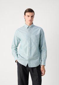 Camicia azzurra chiaro in tessuto morbido, con taschino sul petto e logo ricamato. Maniche lunghe con polsini abbottonati.