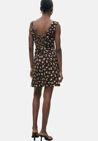 Mustakukka kuviollinen mekko, istuva yläosa, leveät hihnat ja liehukehame. Silkkinen kangas ja joustava rypytys takana.