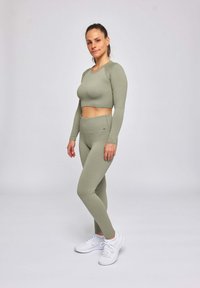 Haut cropped à manches longues en vert olive clair côtelé et leggings taille haute, associés à des chaussures de sport blanches. Texture lisse et design ajusté.