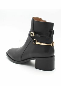 Czarna skórzana botka za kostkę z okrągłym noskiem, grubym obcasem, regulowanym pasek ze złotym akcentem oraz gładką fakturą. Zamek błyskawiczny z tyłu.