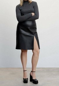 Jupe en cuir noir avec une fente sur le devant, associée à un haut ajusté à manches longues gris foncé. L'ensemble comprend des sandales à talons hauts chunky.