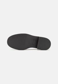 Semelle de chaussure en cuir noir avec une texture lisse, un bout arrondi et un minimum de coutures. Présente une petite section surélevée près du talon.