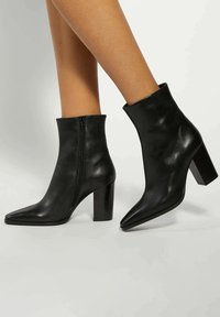 Black leather ankle boots with a pointed toe and block heel. Features a zip closure on the side for easy wear. Smooth texture and minimalist design.