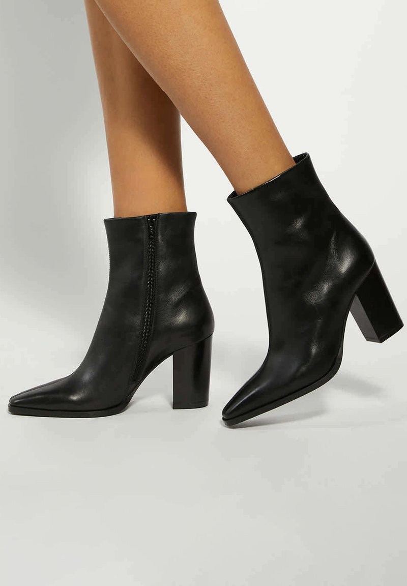 Black leather ankle boots with a pointed toe and block heel. Features a zip closure on the side for easy wear. Smooth texture and minimalist design.