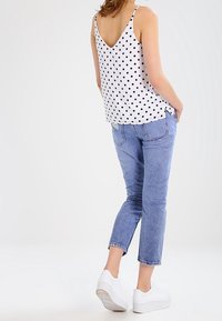 Biała bluzka bez rękawów w czarne kropki, zestawiona z jasnoniebieskimi, krótkimi jeansami i białymi sneakersami na platformie. Prosty design i casualowy fason.