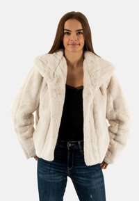 Witte fake bont jas met een brede kraag, met een zachte textuur en een relaxte pasvorm, gecombineerd met donkere jeans en een zwarte top.