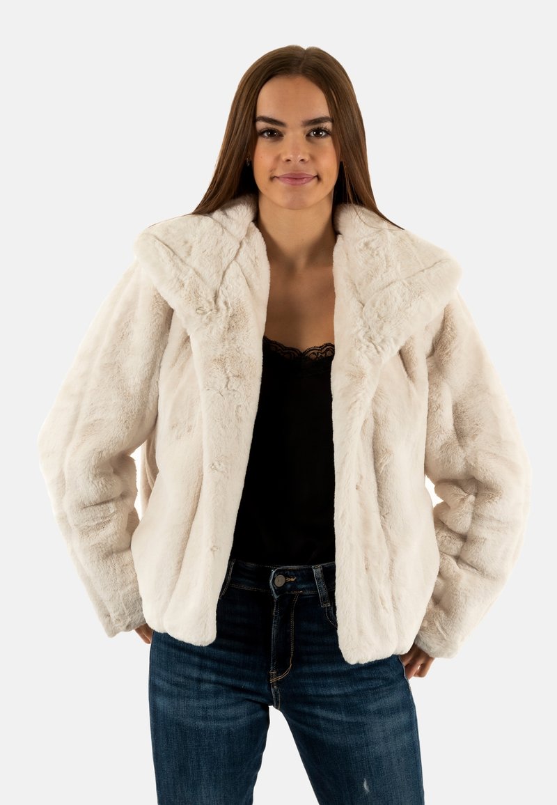 Witte fake bont jas met een brede kraag, met een zachte textuur en een relaxte pasvorm, gecombineerd met donkere jeans en een zwarte top.