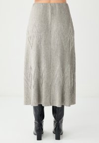 Grau gerippter Midirock mit dezent strukturiertem Muster. Der Rock reicht bis zur Mitte der Wade und wird mit knielangen schwarzen Stiefeln kombiniert.