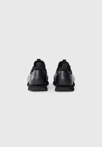 Zwarte sneakers met een soepel leren bovenwerk en een gestructureerde rubberen zool, voorzien van aantrektabs op de hiel en een strak ontwerp.