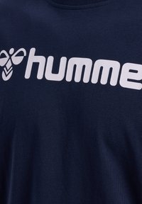 Camiseta de algodón azul marino con un gran logo blanco de "humme" y un gráfico de abeja, con una textura suave y cuello redondo.