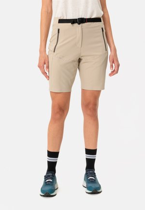 Lichtbeige shorts met een gladde textuur, zwarte ritszakken en een zwarte verstelbare riem. Gepaarde met teal sportchoenen en zwarte gestreepte sokken.