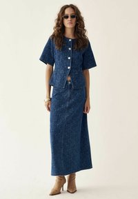 Completo in denim composto da una camicia a maniche corte con bottoni e una gonna lunga, entrambi in un blu scuro con una leggera texture.