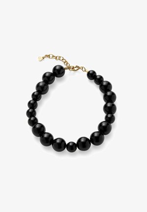 Melna spīdīga aproce ar pakāpeniski palielinātām apaļām pērlēm un zelta toni ķēdes aizdares uz balta fona.