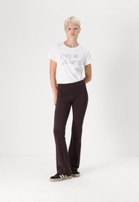 Hvid t-shirt med "Pepe Jeans" i metalfarver, parret med mørkebrun flagrende bukser og sorte sneakers med hvide striber.