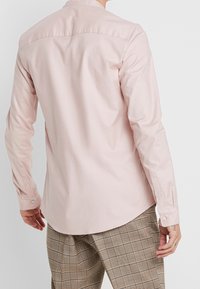 Långärmad skjorta i ljusrosa, figursydd passform, slät textur, knappmanschetter, rundad nederkant, kombinerad med rutiga byxor.