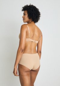 Beige trådløs bh med justerbare stropper og glatt stoff, kombinert med matchende høyt midje undertøy, begge med minimale sømmer.
