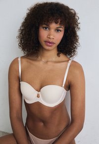 Soutien-gorge rembourré beige avec armatures, bretelles réglables et fermeture à l'avant. Texture lisse, design minimaliste.