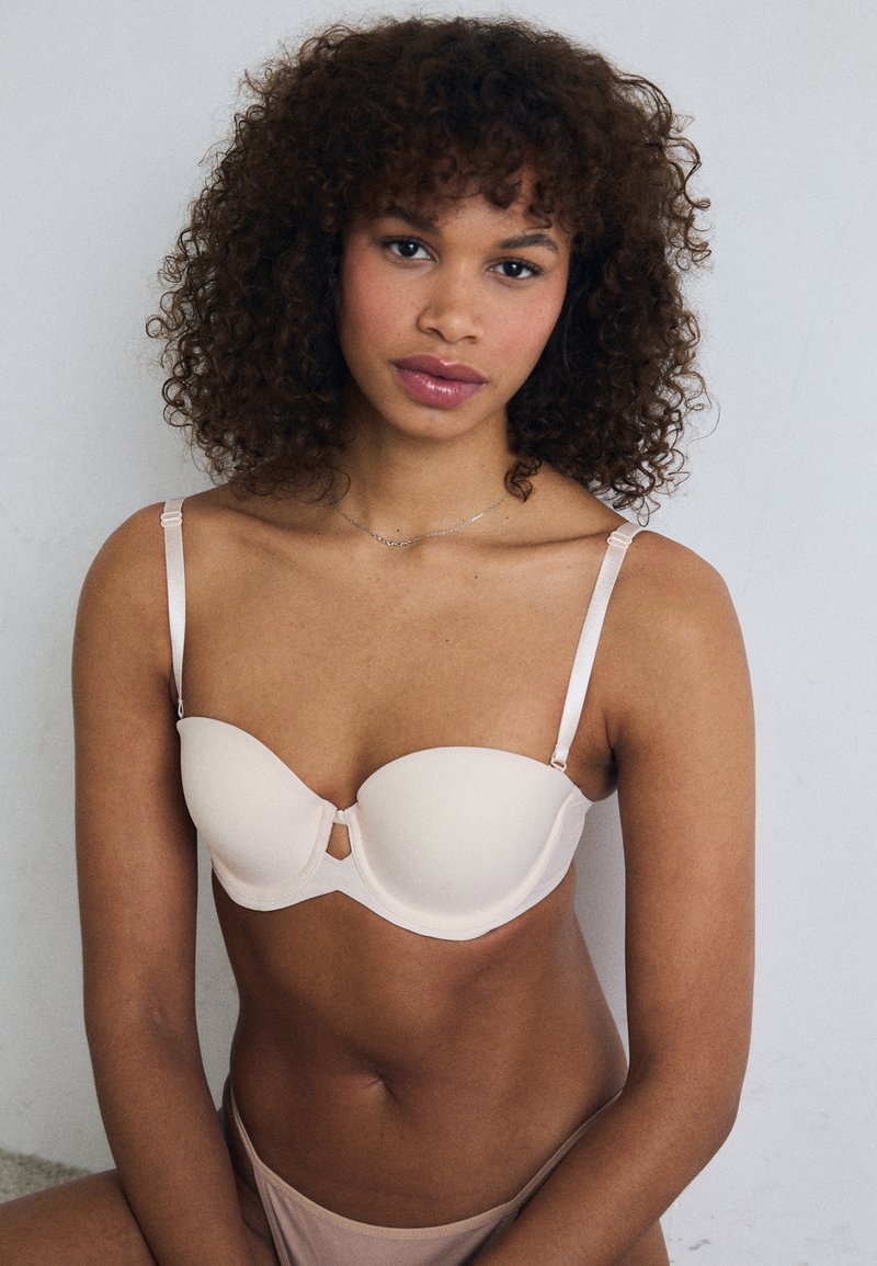 Soutien-gorge rembourré beige avec armatures, bretelles réglables et fermeture à l'avant. Texture lisse, design minimaliste.