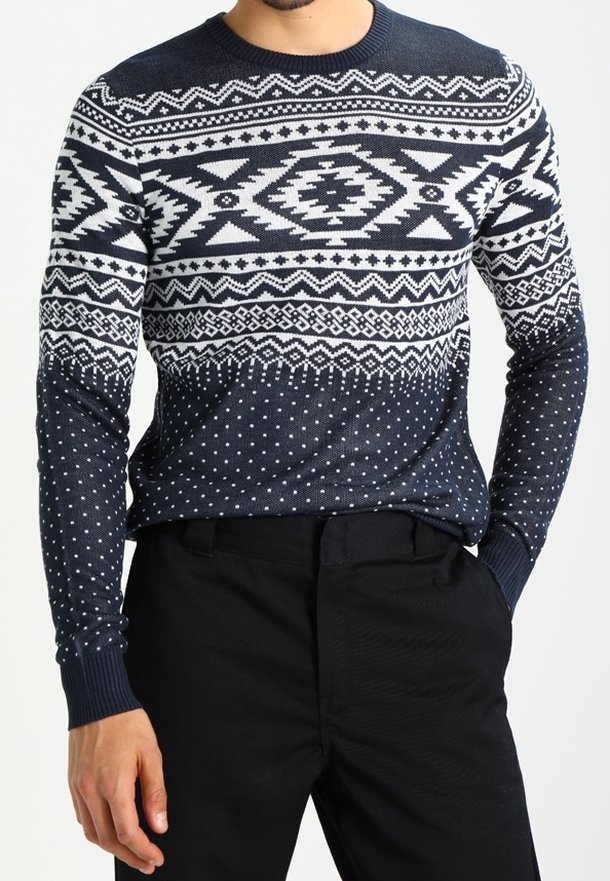 Mörkblå stickad tröja med vita geometriska mönster, inklusive diamanter och prickar, samt ribbade ärmar. I kombination med svarta byxor.