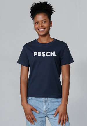 T-shirt marine avec un col rond et des manches courtes, arborant un texte blanc en gras "FESCH." sur le devant. Le tissu semble lisse.