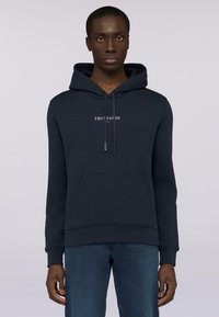 Mörkblå hoodie med kenguruficka, dragsko och tryckt logotyp på bröstet. Tillverkad av ett strukturerat material, med ribbade ärmslut.