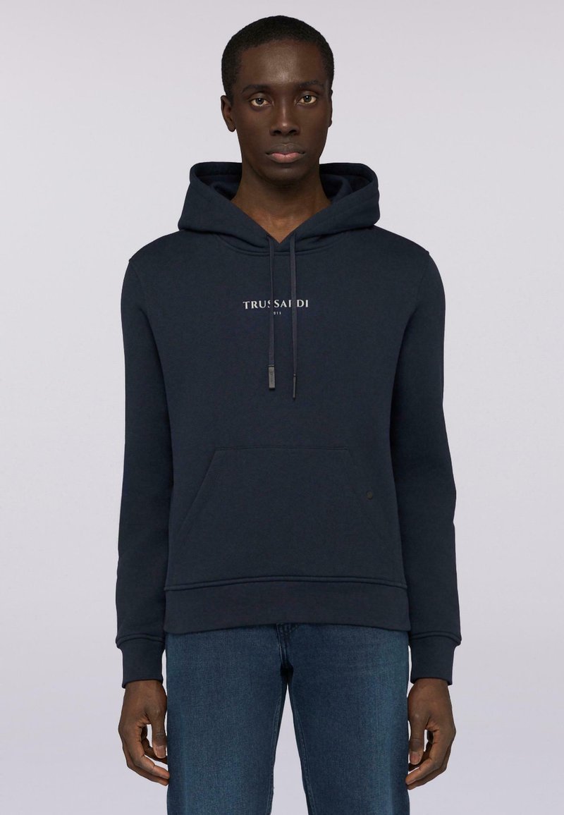 Mörkblå hoodie med kenguruficka, dragsko och tryckt logotyp på bröstet. Tillverkad av ett strukturerat material, med ribbade ärmslut.