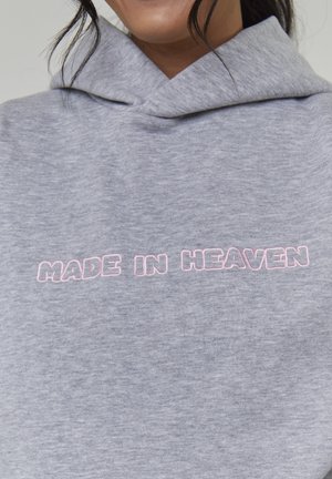 Grauer Hoodie mit weicher Textur, der vorne den Schriftzug "MADE IN HEAVEN" in rosa Stickerei zeigt. Er hat eine lockere, übergroße Passform.