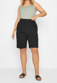 Svarta shorts med elastisk midja och sidofickor, matchade med en ljusgrön ärmlös topp och svarta sandaler. Mjuk tygstruktur.