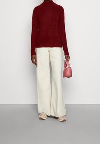 Burgundin merinopaita, vaaleat leveälahkeiset housut, vaaleanpunainen käsilaukku kuvioiduilla hihnoilla ja beige urheilukengät. Tasaiset pinnat kauttaaltaan.