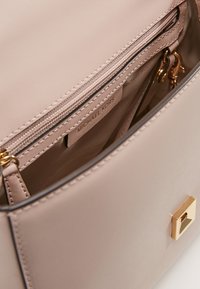 Sac à main beige Michael Kors avec une fermeture à glissière dorée, ouvert pour montrer la poche intérieure zippée et l'étiquette de marque à l'intérieur.