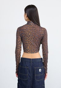 Brun leopardmønstret langærmet top med høj krave og cropped design, parret med en mørk denimnederdel med store lommer.