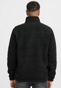 Black fleece jacket with a high collar, textured surface, long sleeves, and a relaxed fit, featuring a simple design and no visible logos.