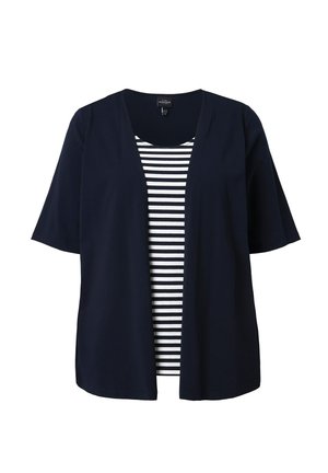 Marineblaue, offen geschnittene Kurzarm-Strickjacke, darüber getragen ein schwarz-weiß gestreiftes Top mit rundem Ausschnitt.
