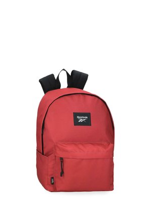 Mochila roja Reebok con correas negras, bolsillo frontal con cremallera y parche con el logotipo de Reebok en la parte superior delantera, mostrada sobre fondo blanco.