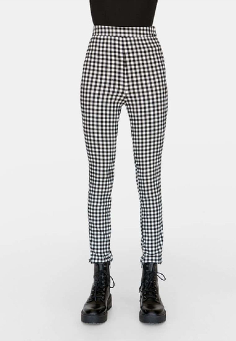 Pantalon slim à carreaux noir et blanc associé à des bottines noires à lacets sur une personne portant un haut noir.
