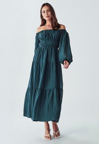 Maksi haljina bez naramenica u tamno tirkiznoj boji, s naboranim korzetom, dugim napuhanim rukavima i suknjom u slojevima s naboranom teksturom.