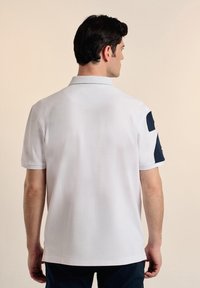 Camisa polo blanca con acentos en azul marino en los hombros, mangas cortas y un cuello clásico, hecha de un material texturizado y transpirable.
