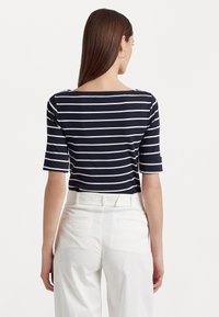 Top rayé marine avec des rayures blanches, encolure bateau et manches à mi-longueur. Assorti avec un pantalon blanc ajusté, vue de dos.