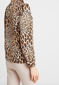 Lynxprint button-up skjorte i beige og brune nuancer med lange ærmer, krave og samlede detaljer ved manchetterne. Glat, let stof.