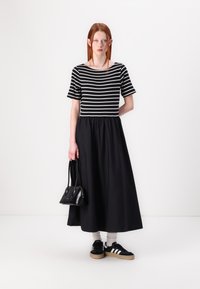 Svart-hvitt stripete topp med korte ermer, paret med et langt svart skjørt. Tilbehør inkluderer en svart håndveske og svarte sko med hvite striper.