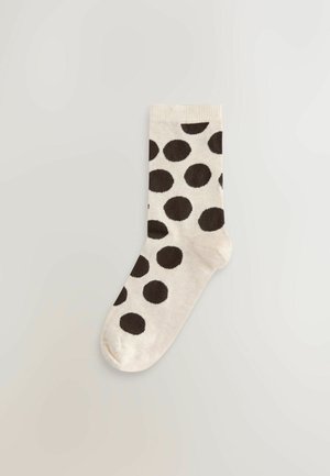 Beige sok med store brune polkaprikker, ribbet tekstur, rund tå og elastisk kant, designet til komfort og pasform.