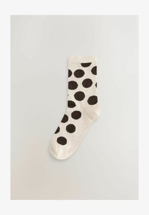 Beżowa skarpeta z dużymi brązowymi groszkami, prążkowaną fakturą, zaokrąglonym noskiem i elastycznym mankietem, zaprojektowana dla komfortu i dopasowania.