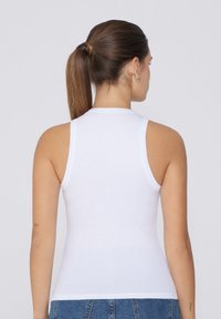 Top bianco a coste senza maniche con scollo tondo, design aderente e superficie liscia, mostrato di spalle con jeans in denim blu.