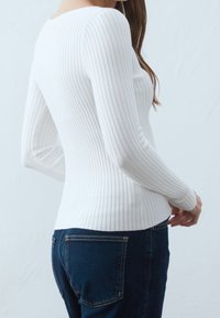 Vit ribbad långärmad topp med båthals, figursydd design och subtil textur, kombinerad med mörkblå jeans.