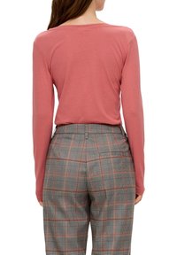 Långärmad, rosa topp i kombination med grå rutiga byxor med orange detaljer, stiliserad med en skräddarsydd passform och midjeband.