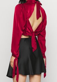 Červená saténová krátká blůza s dlouhými rukávy, zavazováním na zádech a otevřeným designem zad, spárovaná s černou saténovou širokou sukní.