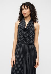 Robe noire à col licou avec des rayures verticales blanches, présentant un décolleté drapé, une taille ceinturée et une coupe ample. Tissu lisse à la texture douce.