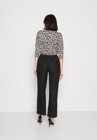 Luipaardprint top met driekwartmouwen, gecombineerd met high-waisted zwarte broek. De broek heeft een losse pasvorm en een gestructureerde stof.